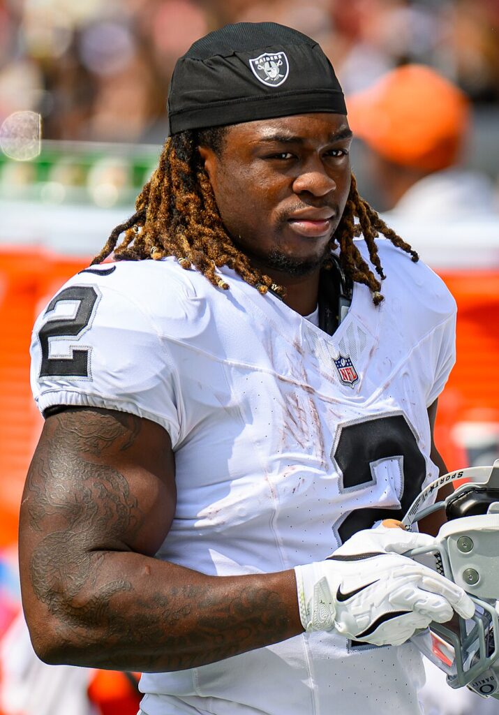 Ashton Jeanty in a white Las Vegas Raiders No. 2 jersey holding his helmet on the sideline