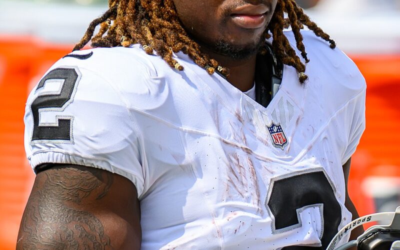 Ashton Jeanty in a white Las Vegas Raiders No. 2 jersey holding his helmet on the sideline