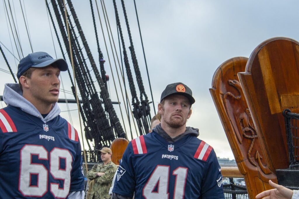 Brenden Schooler, wearing a navy Patriots No. 41 jersey and a cap, with a teammate aboard USS Constitution