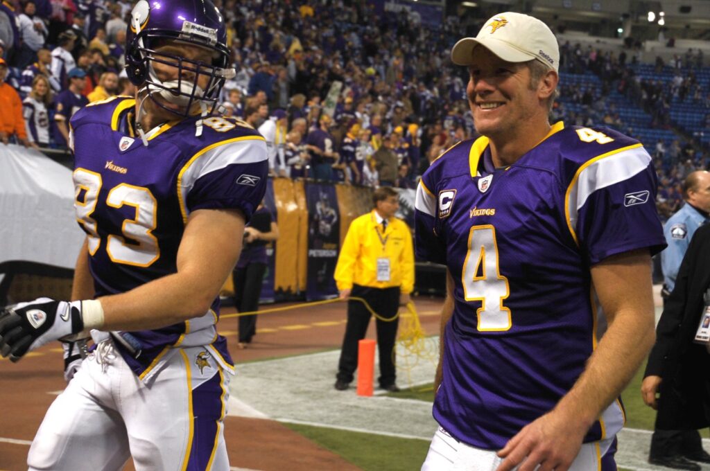 Minnesota Vikings quarterback Brett Favre in a purple number 4 jersey and white cap smiling on the field next to tight end Jeff Dugan
