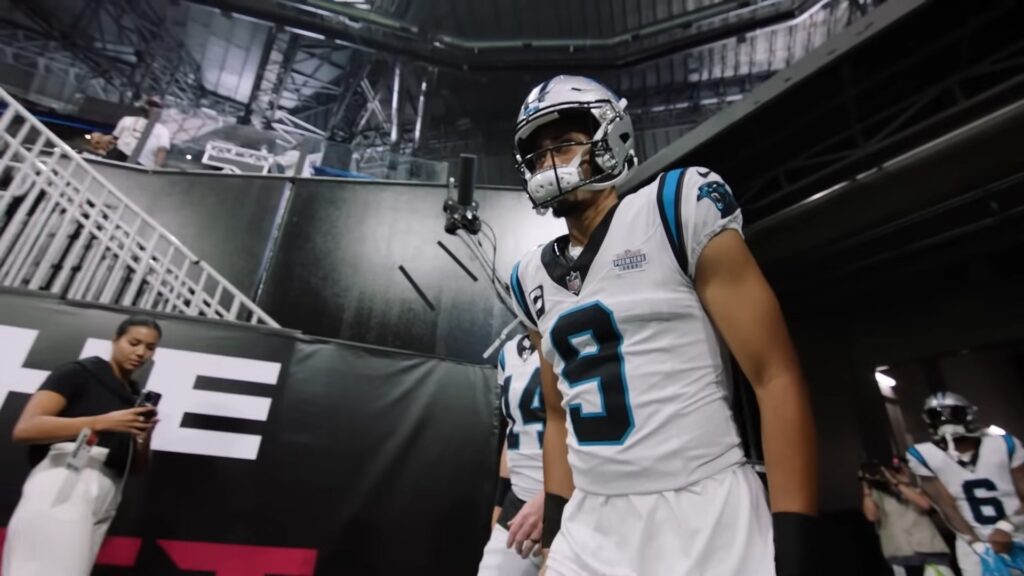 Bryce Young in a white Carolina Panthers No. 9 jersey and silver helmet walking out of the stadium tunnel