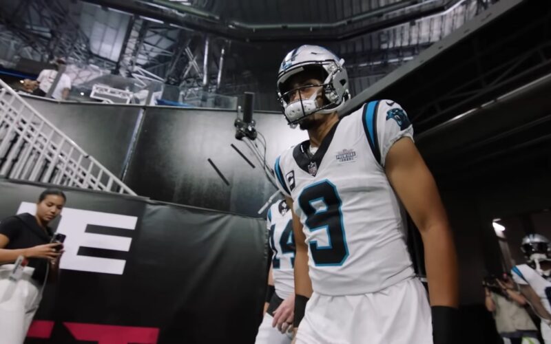 Bryce Young in a white Carolina Panthers No. 9 jersey and silver helmet walking out of the stadium tunnel