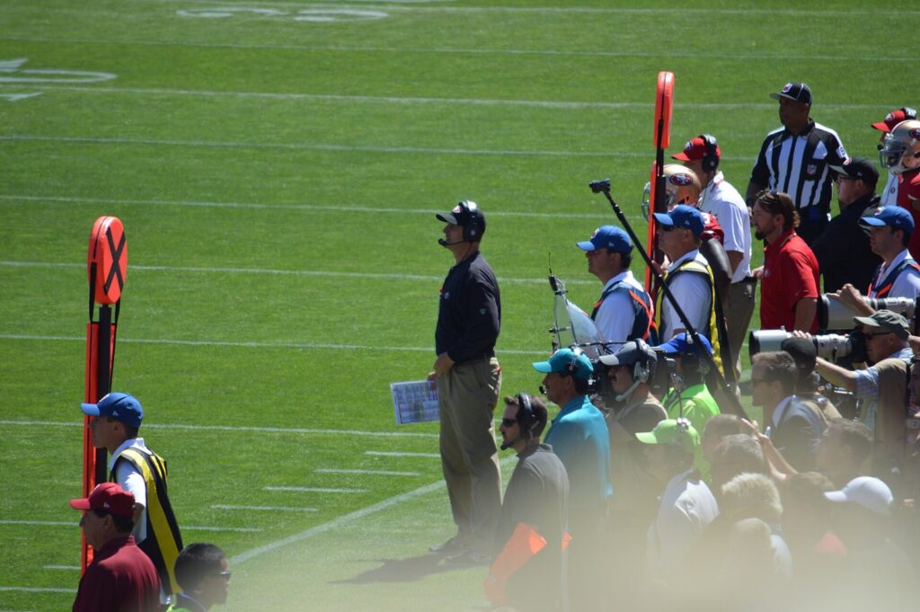 Jim Harbaugh in a dark 49ers top and headset standing on the sideline during a game