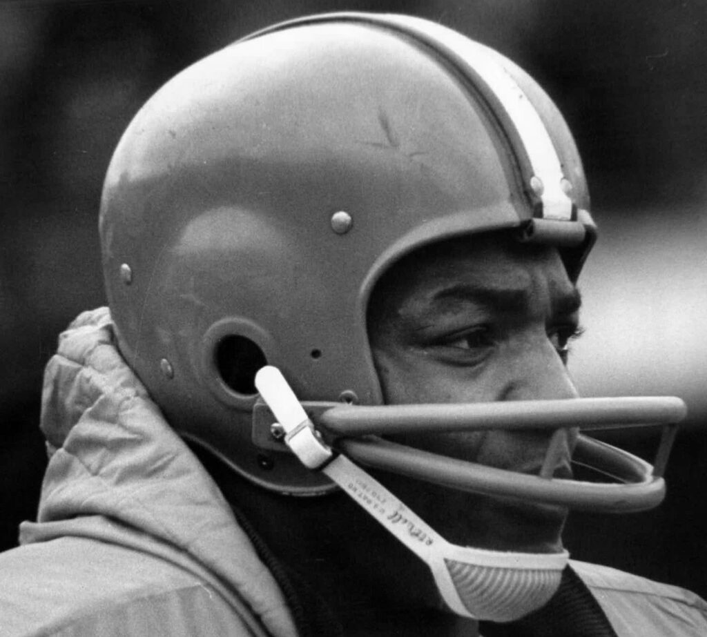 Black-and-white close-up of Cleveland Browns fullback Jim Brown in his helmet on the sideline