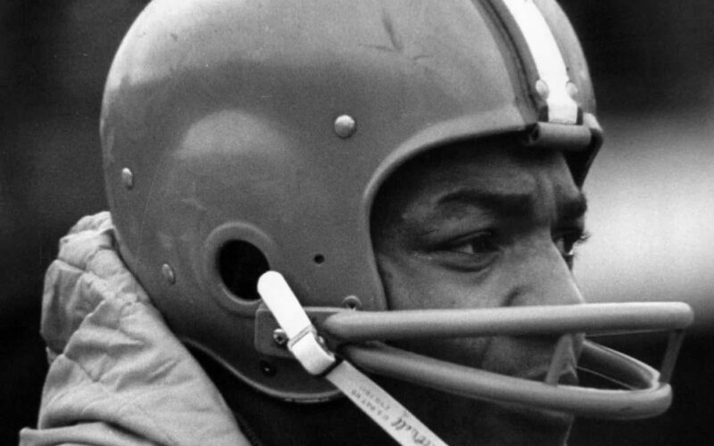 Black-and-white close-up of Cleveland Browns fullback Jim Brown in his helmet on the sideline