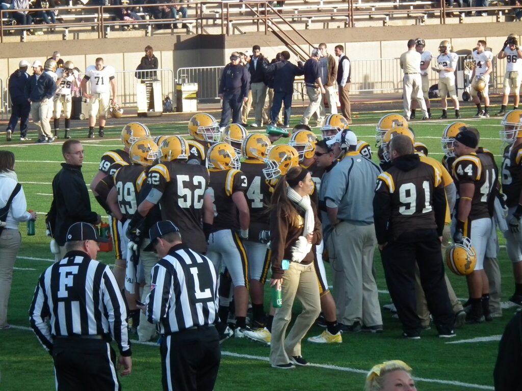 Football players in a huddle near coaches and officials on the sideline