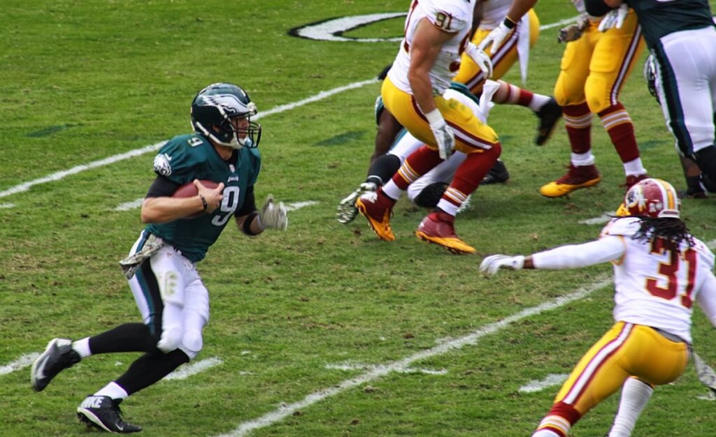 Philadelphia Eagles quarterback Nick Foles, wearing green number 9, runs with the ball as Washington defenders in white and burgundy chase him
