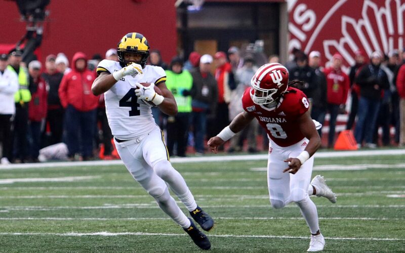 Nico Collins, wearing Michigan’s white No. 4 uniform, runs with the football beside an Indiana defender.