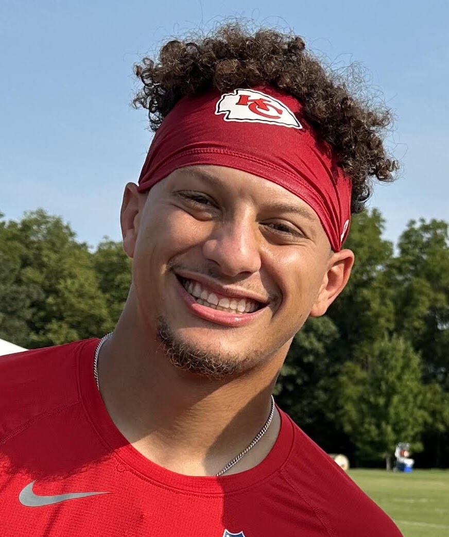 Patrick Mahomes in a red Chiefs jersey holding a football on the field