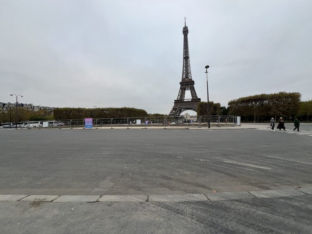 Place Jacques-Rueff at the southern end of the Champ-de-Mars in Paris under a grey sky, with the Eiffel Tower behind