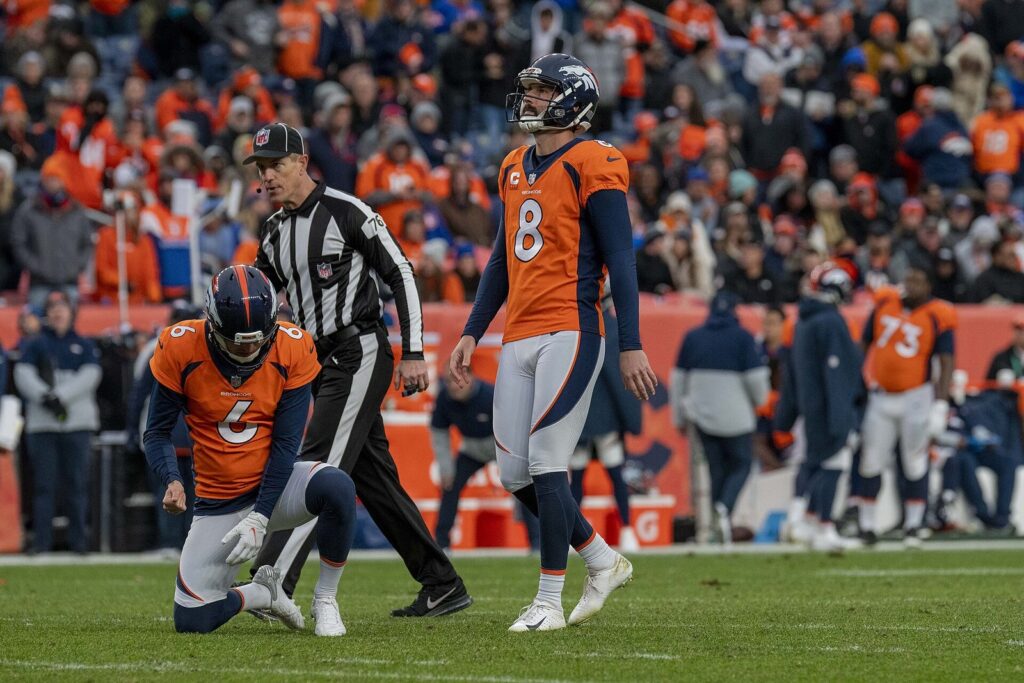 Brandon McManus, No. 8, watches a kick for the Denver Broncos in 2021 as his holder kneels