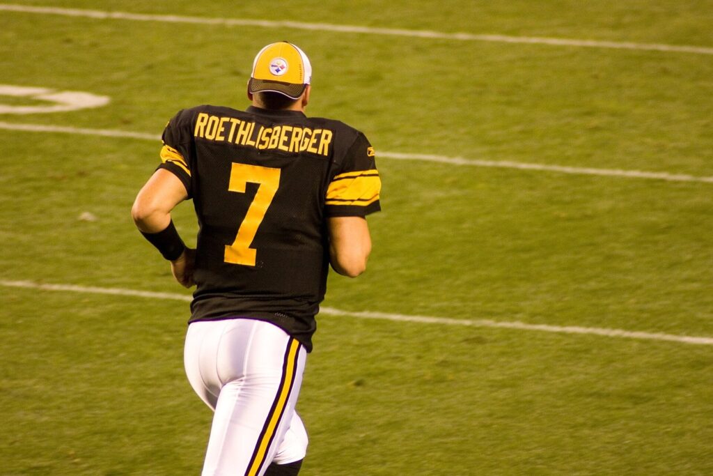 Ben Roethlisberger in a black number 7 Steelers throwback jersey jogging on the field, seen from behind