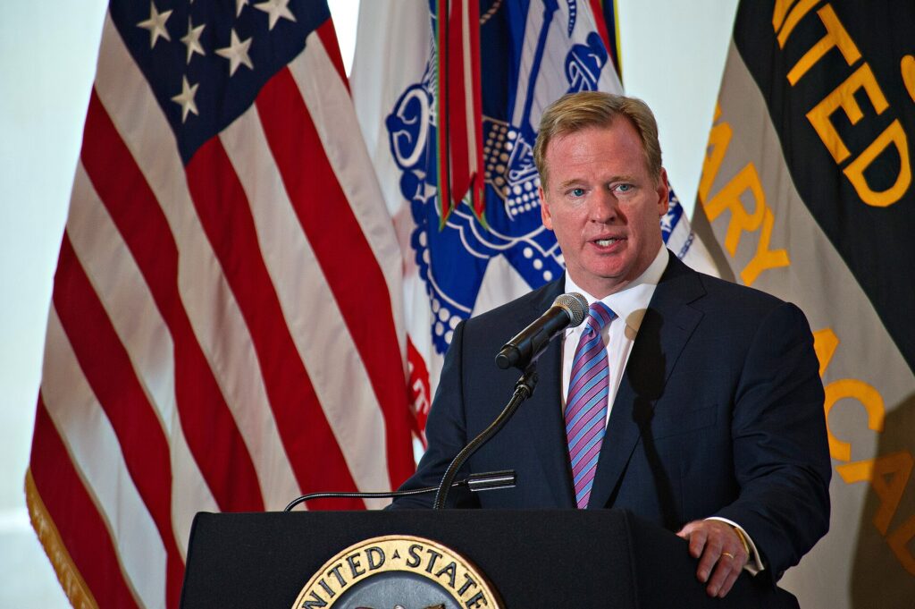 Roger Goodell speaking at a podium in front of U.S. and Army flags