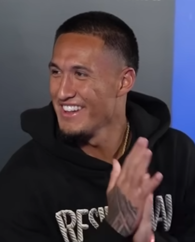 Tetairoa McMillan smiles and claps while wearing a black hoodie in an archival interview video.